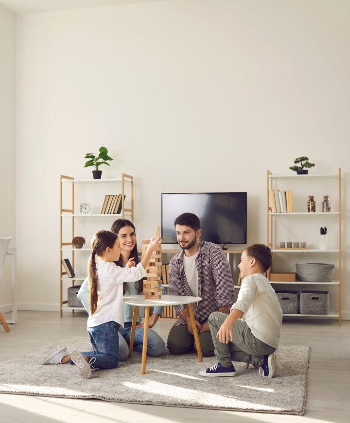 Happy family father mother and two children sitting on floor and playing at home together during weekend. Family spending happy time at home and having fun with children concept